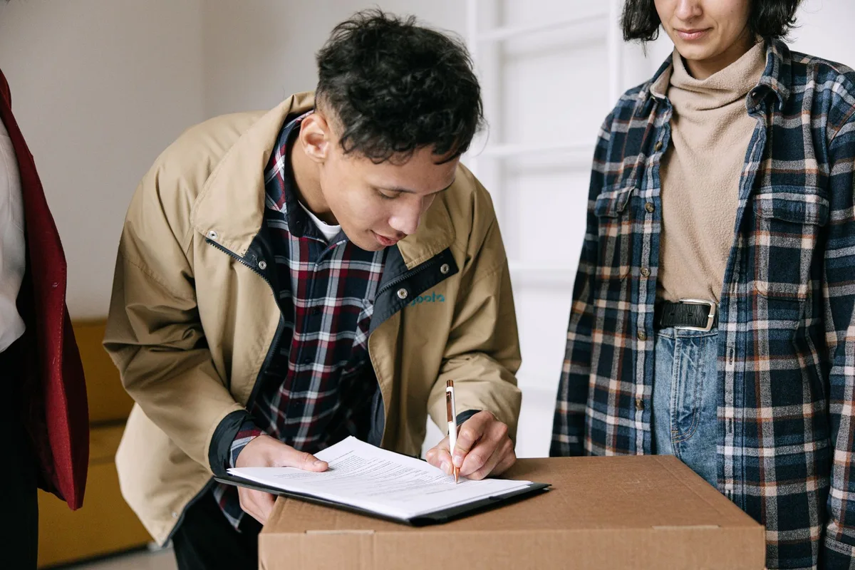 Client qui signe un document de déménagement posé sur un carton