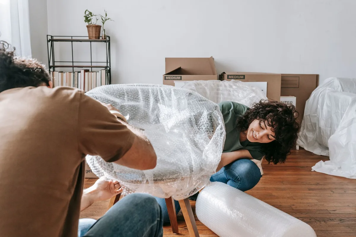 Couple qui emballe un fauteuil dans du papier bulle avant de le stocker
