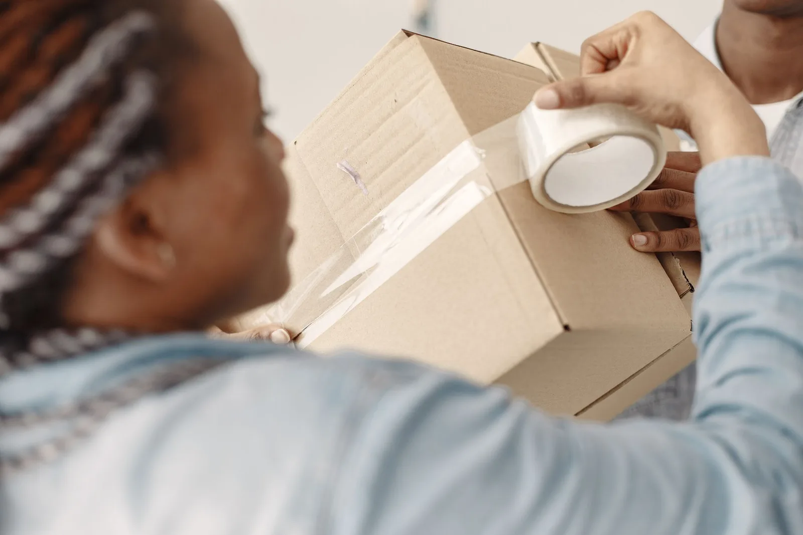 Mains qui ferment un carton de déménagement avec du ruban adhésif