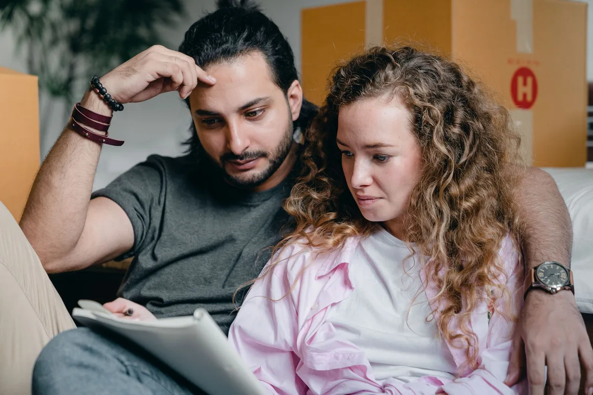 Couple qui consulte ses notes de déménagement assis au milieu des cartons